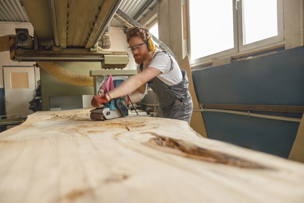 Bearded male wood worker using electric sander for wood. Carpentry workshop. High quality photo, handyman near me